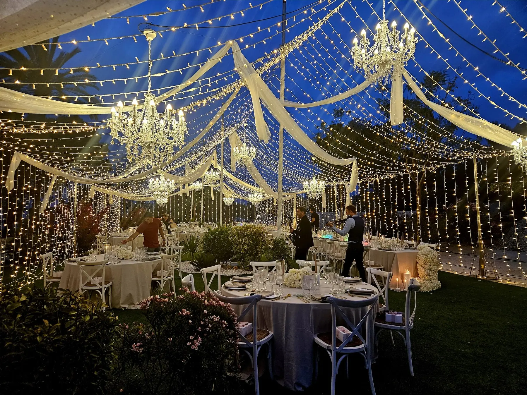 El interior de la carpa por la noche, con lámparas de araña, telas blancas y cortinas de luces sobre las mesas del banquete